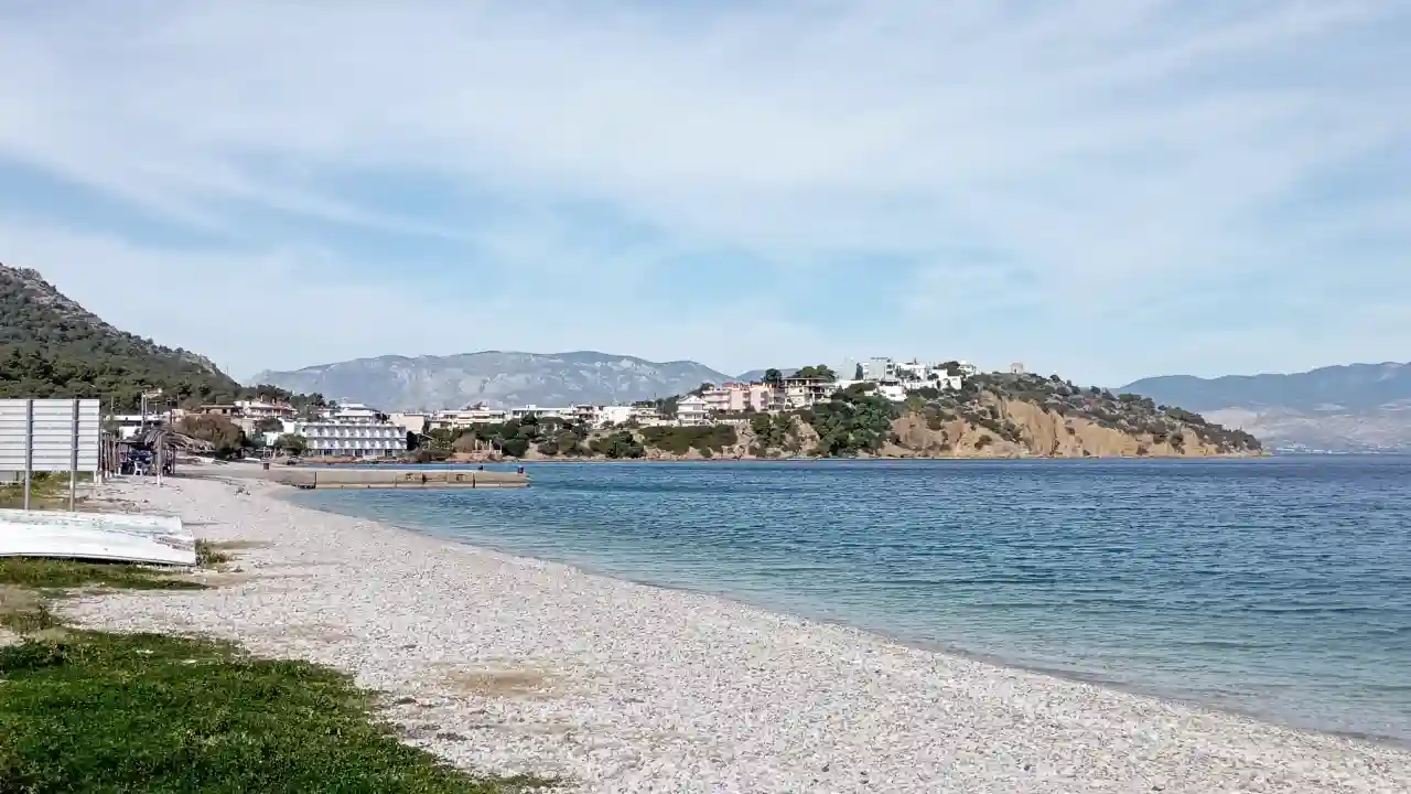 A photo of a beach with soft, white sand and turquoise water. Lush green mountains covered in mist rise up in the background.