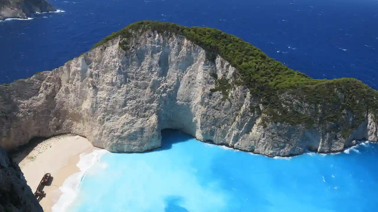 A view of Navagio Beach on the Greek island of Zakynthos. The beach is a popular tourist destination and is known for its white sand, clear turquoise waters, and the shipwreck of a smuggler's ship that is now stranded on the beach.