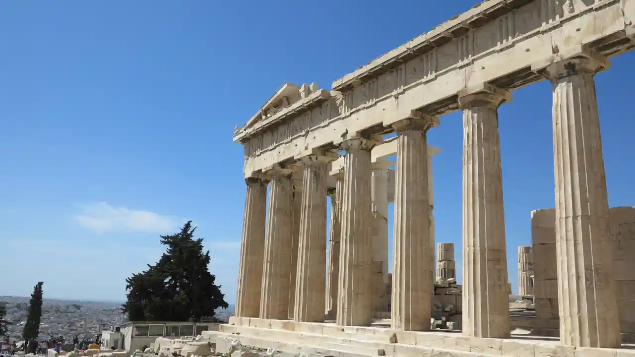 A close-up view of the eastern facade of the Parthenon, a temple on the Acropolis of Athens, Greece. The Parthenon is bathed in sunlight, and the sky is blue and clear.