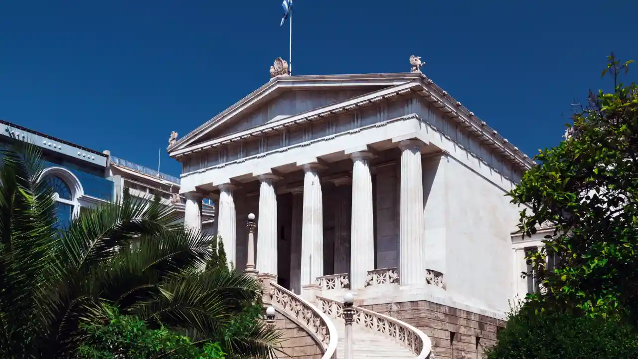 A photo of the National Library of Greece, a neoclassical building with a grand staircase leading up to its entrance. The library is located in Athens, Greece.