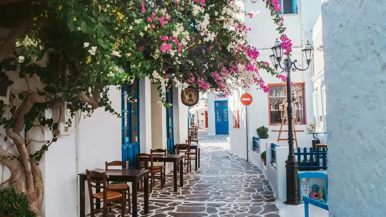 A sunny outdoor cafe with tables and chairs on a narrow Greek street