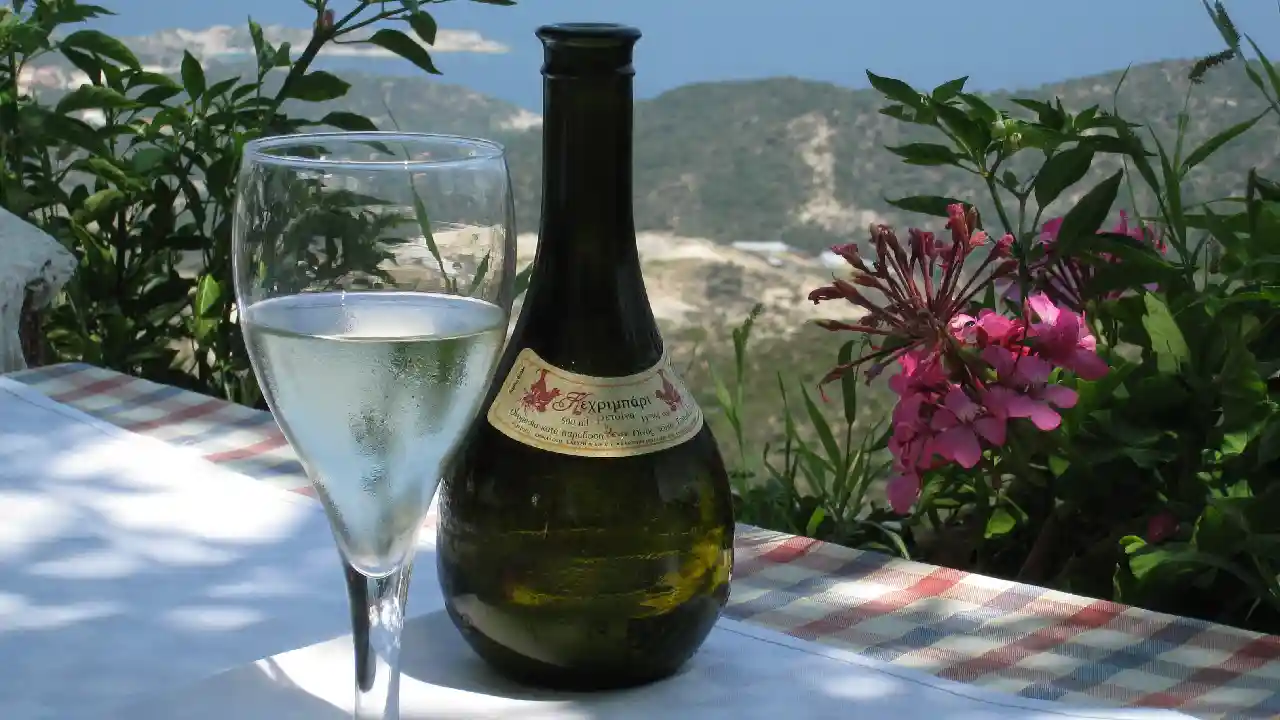 A table setting with a bottle and a glass of Kechribari Retsina wine. There is also a flower arrangement in a vase on the table.