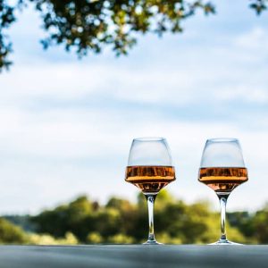 Two wine glasses sit on a white table in front of a green field.