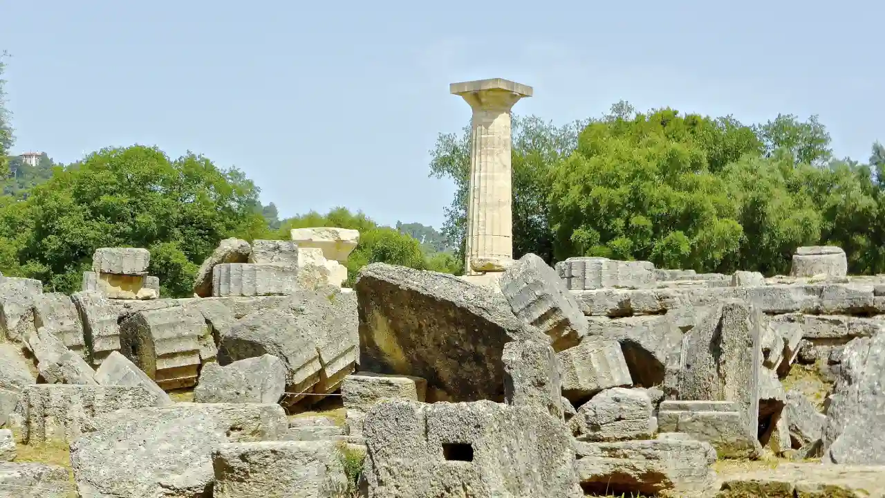 Temple of Zeus at the archaeological site of Olympia in Greece. The temple is in ruins, with only a single pillar remaining standing.