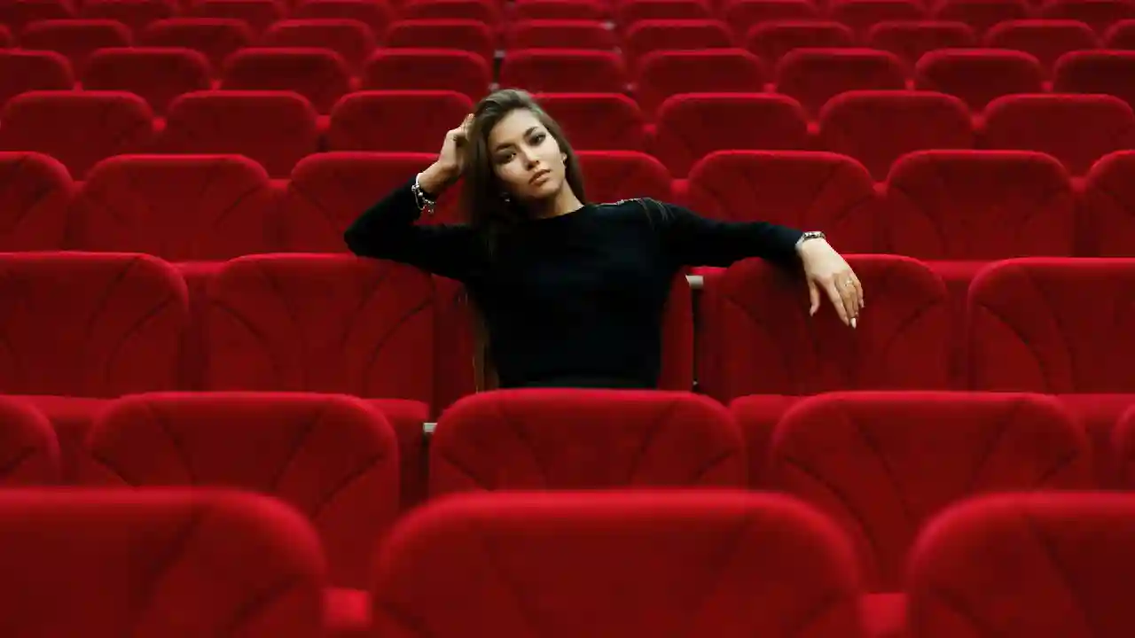 a woman sits in the red seats of a theater