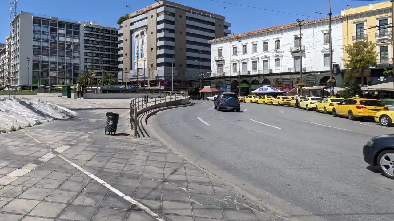 A row of yellow taxi cabs parked curbside in front of the Hondos Center in Omonoia Square, Athens, Greece.