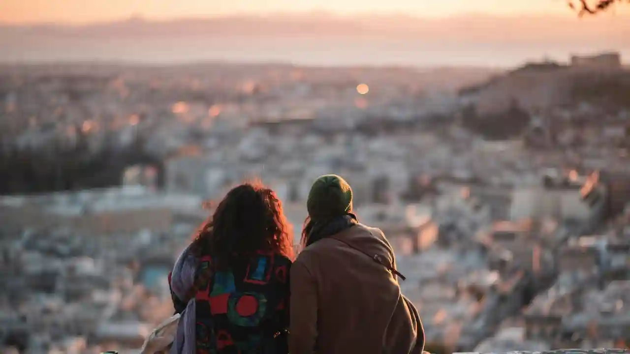 two people sit on a stone wall in Lycabettus, Athens, looking down on the city