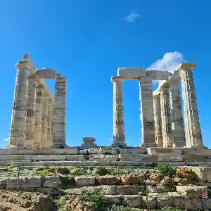 Ruins of the Temple of Poseidon at Cape Sounion, Greece. The temple stands on a cliff overlooking the Aegean Sea. The columns are weathered and the sky is a clear blue.