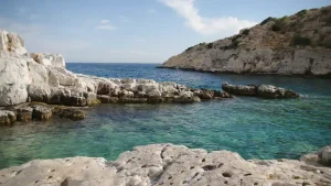 A secluded cove with crystal-clear turquoise water surrounded by white cliffs. The sky is a clear blue with some clouds.