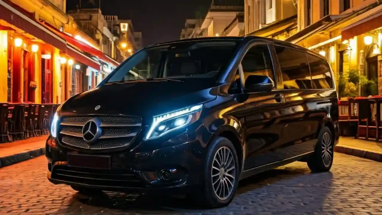 A sleek black Mercedes-Benz V-Class minivan parked on a cobblestone street in Athens, Greece. The car's elegant design and illuminated headlights create a sophisticated ambiance, perfect for a stylish night out in the city.