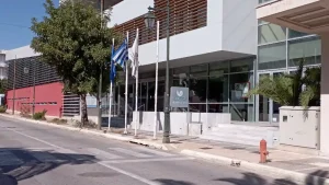 The Loutraki Thermal Spa building in Loutraki, Greece. The building is a modern structure with a glass facade and a Greek flag flying outside.