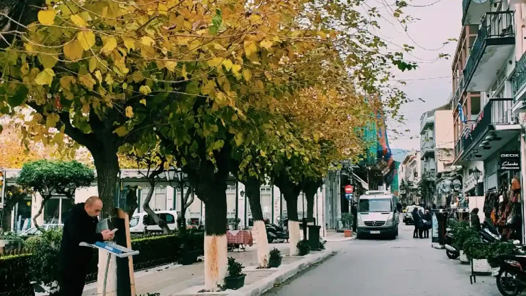 A photo of a crowded street in the Plaka district of Athens, Greece. The street is lined with shops, restaurants, and cafes, and is filled with people walking and browsing.