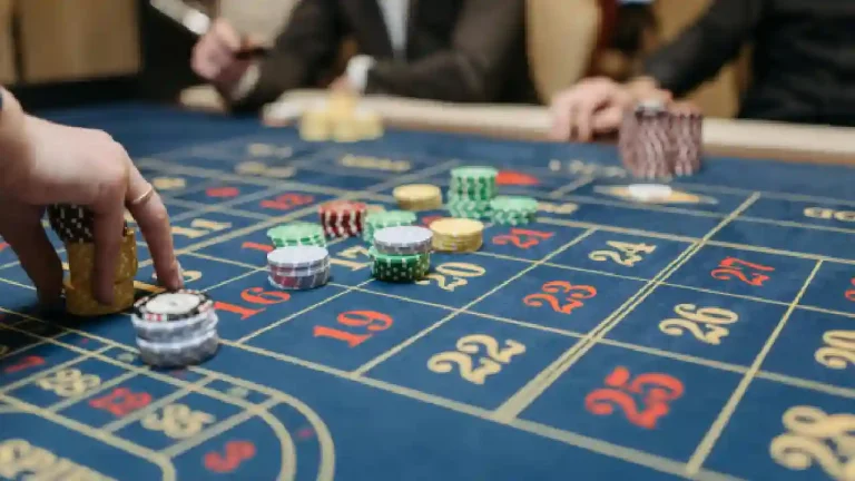 A close-up image of a roulette table in a casino. Chips of various colors are placed on the table, with a player's hand reaching to place a bet.