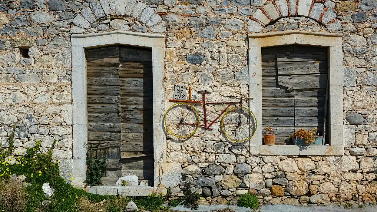 A charming stone building with a weathered wooden door and window shutters. A vintage bicycle is creatively mounted on the wall, adding a touch of whimsy to the scene.