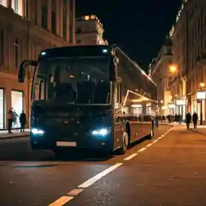 A black coach bus driving down a city street at night. The street is lined with buildings and pedestrians are walking on the sidewalk