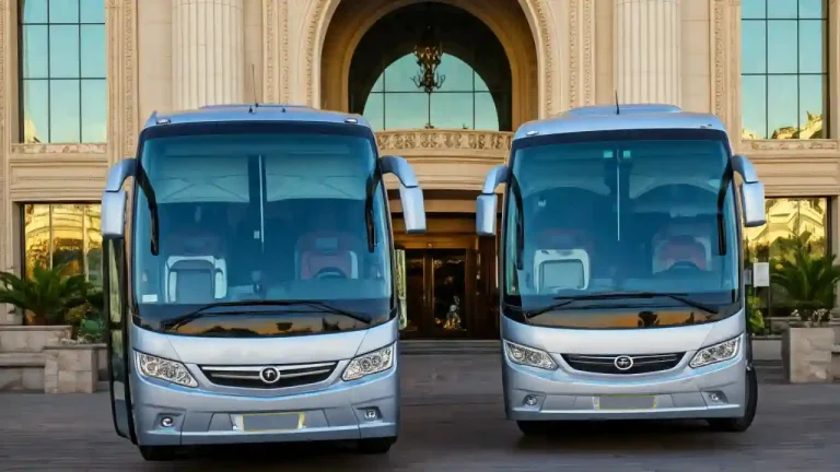 Two modern and luxurious coaches parked in front of a grand hotel entrance. The coaches are sleek and stylish, exuding an air of sophistication.